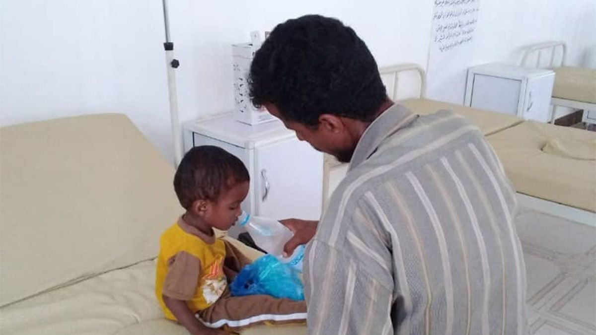 Ein Mann gibt einem an Cholera erkrankten Kind Trinkwasser, damit es nicht dehydriert.
